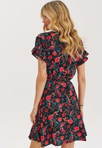 Černé květinové šaty s krátkými volánovými rukávy, zdobené červenými a modrými květinovými vzory. Materiál vypadá lehce a splývavě, stažený v pase.