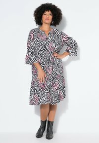 Vestido con estampado de cebra en negro, blanco y rosa, con mangas campana de tres cuartos, abotonadura frontal y bajo con volantes, combinado con botines negros con tachuelas.