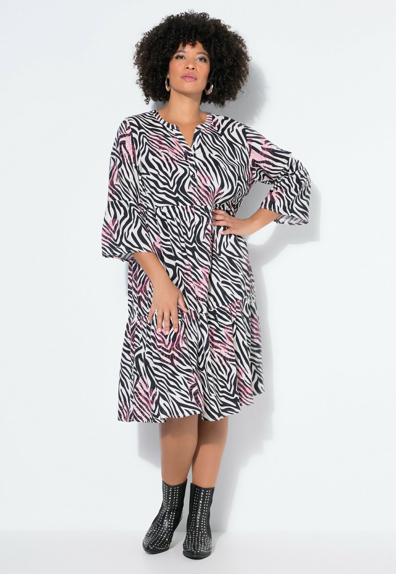 Vestido con estampado de cebra en negro, blanco y rosa, con mangas campana de tres cuartos, abotonadura frontal y bajo con volantes, combinado con botines negros con tachuelas.