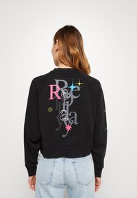 Felpa nera con grafiche testuali colorate e astratte sulla parte posteriore e sulle maniche. Realizzata in tessuto morbido, con un design cropped e polsini a costine.