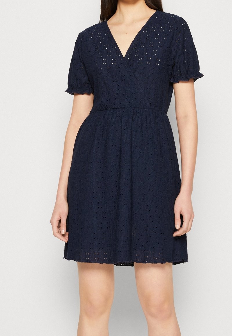 Vestido azul marino hecho de tela de ojo de perdiz. Presenta un escote en V, mangas cortas abullonadas, cintura ajustada y una falda acampanada, con un patrón texturizado.