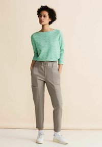Grön texturerad tröja med vid halsringning, tillsammans med ljusgrå tapered byxor med sidofickor och elastisk midja. Vita sneakers.