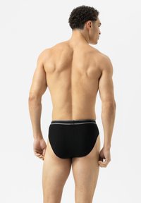 Schwarze gerippte Unterwäsche mit einem grauen Bund, die eine enge Passform und glatte Textur zeigt, von hinten auf einem schlichten weißen Hintergrund betrachtet.