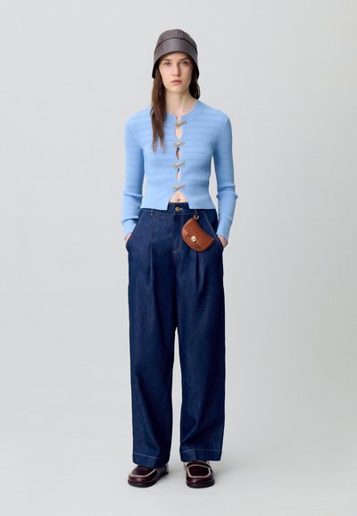 Cardigan a coste blu chiaro con bottoni, abbinato a pantaloni larghi in denim scuro e borsa marrone. Indossato con un cappello a secchiello marrone e scarpe.