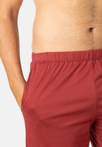 Shorts rouges en coton avec une taille élastique et des poches latérales, présentant une texture lisse et une coupe décontractée.