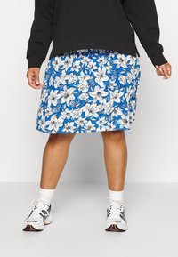 Saia floral com fundo azul, apresentando lírios brancos. O tecido parece leve e fluido, com um cós elástico.