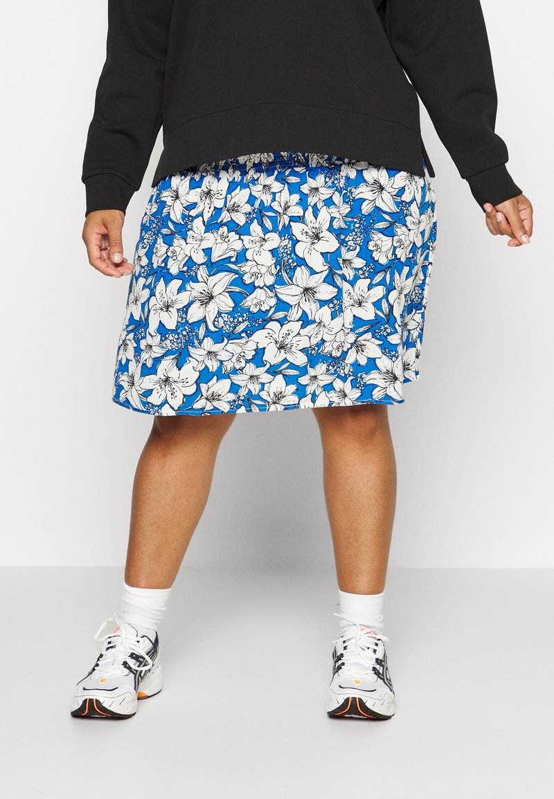 Saia floral com fundo azul, apresentando lírios brancos. O tecido parece leve e fluido, com um cós elástico.