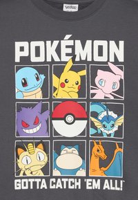 Szürke póló, amelyen négyzetekben Pokémon karakterek láthatók, köztük Pikachu, Squirtle és Mew, középen egy Pokéballal és a "Gotta Catch 'Em All!" felirattal.