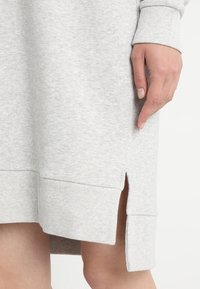 Hellgraues Sweatshirtkleid mit gerippten Bündchen und Saum, ausgestattet mit seitlichen Schlitzen für mehr Bewegungsfreiheit und einer weichen, strukturierten Stoffoberfläche.