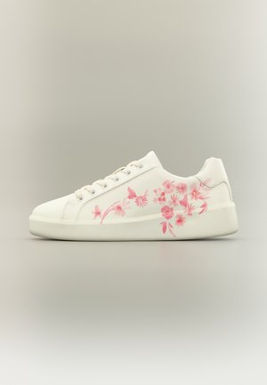 Baskets blanches avec un motif floral rose sur le côté, fermeture à lacets, semelle plate et finition lisse sur un fond neutre.
