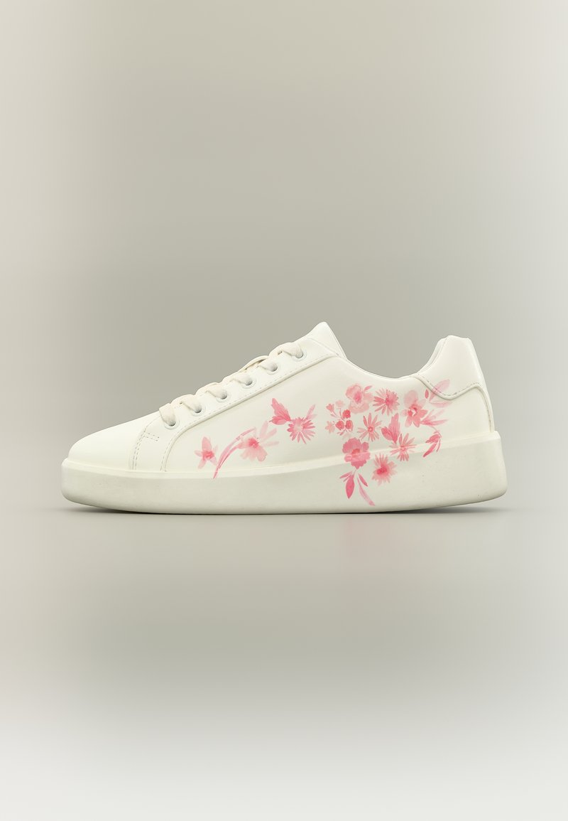 Λευκό αθλητικό παπούτσι με ροζ λουλουδάτο σχέδιο στο πλάι, κορδόνια, επίπεδη σόλα και λεία επιφάνεια σε ουδέτερο φόντο.