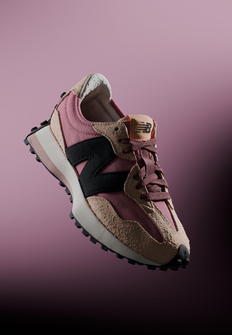 Růžové a béžové tenisky New Balance s černým logem a texturovanou podešví, nakloněné proti pozadí s gradientem růžové barvy.