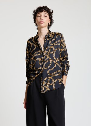Black satin shirt with golden chain pattern, collared, buttoned, relaxed fit, and long sleeves. Paired with loose black trousers.