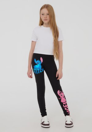Leggings neri con disegni di personaggi dei cartoni animati blu e rosa, con il testo "STITCH" e "ANGEL" stampato sul davanti.