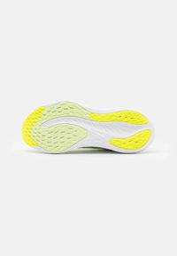 Sole di scarpa sportiva bianca con un motivo testurizzato in giallo e verde. Il design presenta forme esagonali e ondulate per migliorare la trazione.