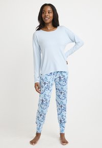 Ljusblå långärmad topp med rundad halsringning, tillsammans med mönstrade blå pyjamasbyxor med blommor och snöflingor.