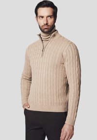 Beżowy sweter z dzianiny warkoczowej z wysokim kołnierzem i zamkiem błyskawicznym. Żebrowany dół i mankiety, średniej grubości materiał, wzór teksturowany.