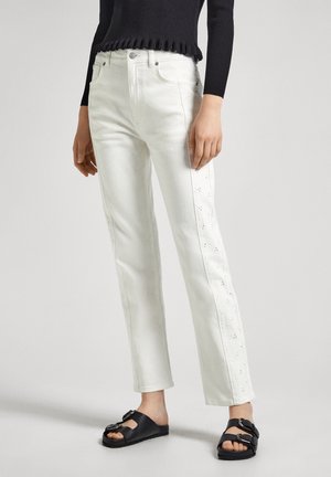 Jean en denim blanc avec des détails brodés sur les côtés, coupe droite, taille haute, associés à des sandales noires à enfiler avec une boucle.