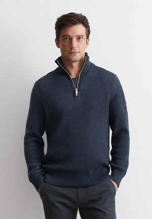 Navy knit pullover with a quarter-zip collar, textured fabric, ribbed cuffs, and waistband. Features a patch detail on the left sleeve.