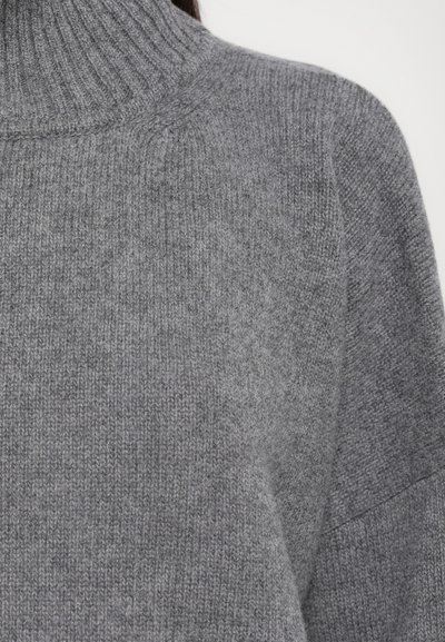 Nahaufnahme eines weichen, grauen Strickrollkragens mit geripptem Kragen und strukturierter Strickmuster auf Schulter und Brust.