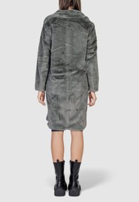 Lungo cappotto oversize grigio in pelliccia sintetica con collare a revers, caratterizzato da una morbida texture e un orlo dritto. Abbinato a stivaletti neri con suola spessa.