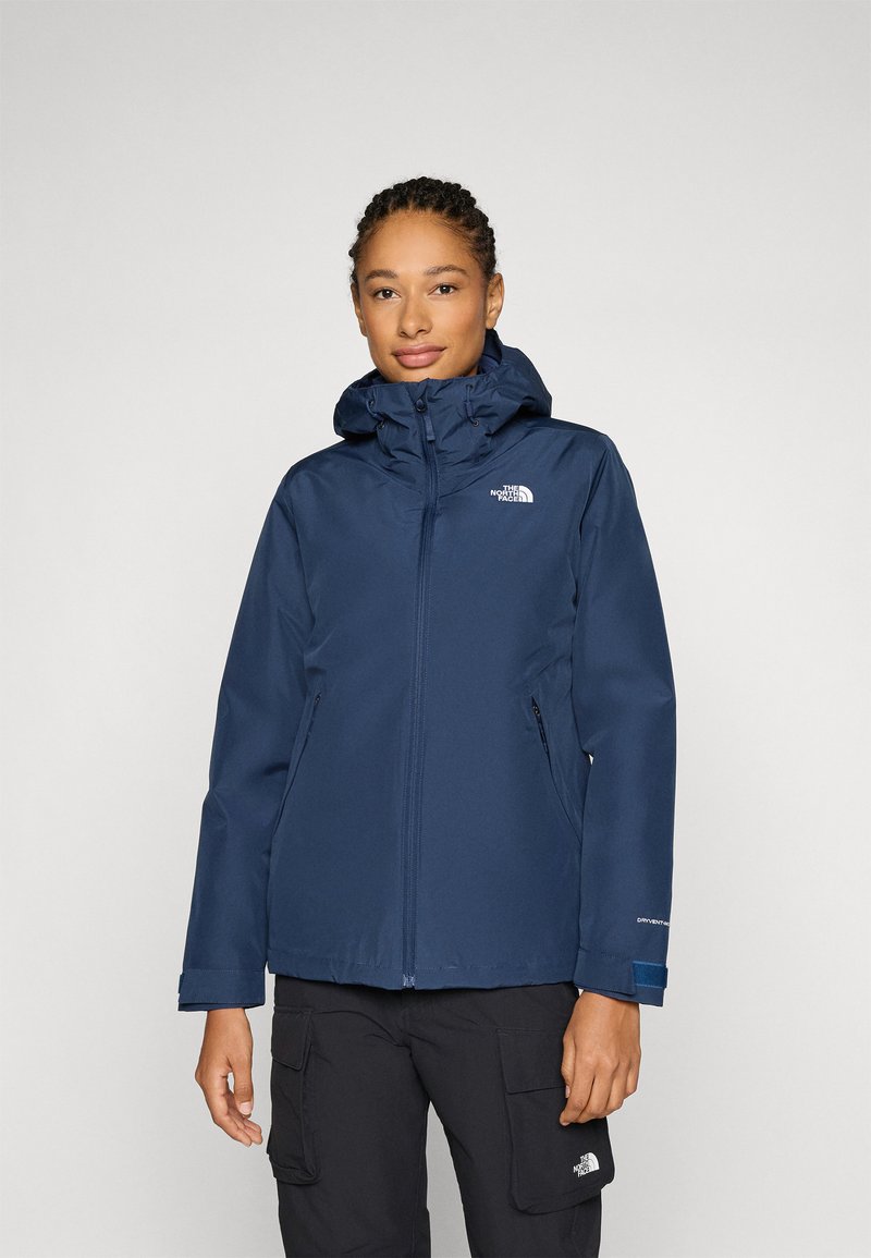 Veste imperméable bleu marine avec capuche, fermeture éclair sur le devant et poches latérales. Fabriquée avec un tissu résistant et dotée d'un logo sur la poitrine gauche.