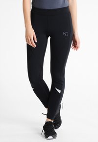 Černé sportovní legíny s přiléhavým střihem, s texturovanými švy a reflexními detaily na dolních nohavicích.