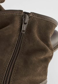 Botte de cheville en suede marron avec une fermeture éclair latérale YKK, des accents en cuir lisse et des coutures marquées le long des bords.