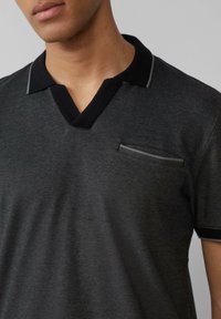 Polo a manica corta grigio scuro con colletto nero e una piccola tasca sul petto. Presenta un tessuto texturizzato e dettagli di cucitura a contrasto.