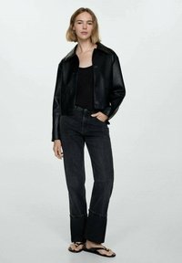 Black faux leather cropped jacket with a collared neck, paired with high-waisted dark jeans. Flat sandals complete the outfit.