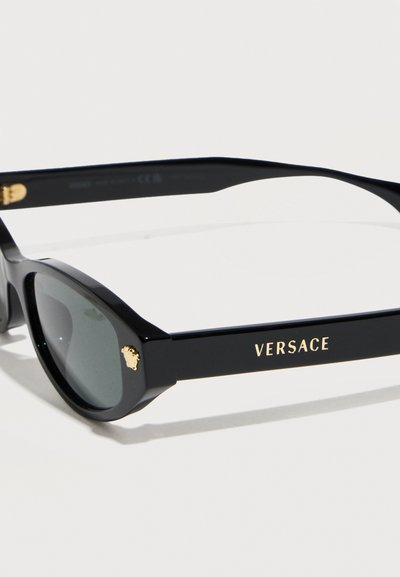 Μαύρα γυαλιά ηλίου Versace με σκούρους φακούς, που διαθέτουν χρυσό λογότυπο Medusa στη γωνία μπροστά και το όνομα Versace στο πλευρικό μπράτσο.