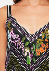 Tecido preto com um design em V, apresentando padrões florais coloridos em rosa, laranja e branco, emoldurado por realces em branco e rosa.