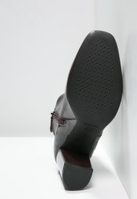 Skórzany botek na obcasie, nachylony w górę, ukazujący teksturowaną gumową podeszwę z okrągłym wzorem grip i detalem bocznego zamka.