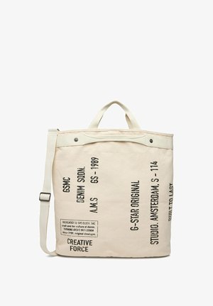 Borsa tote in tela crema con scritta nera stampata, doppie maniglie e tracolla regolabile, con dettagli di marchio e design.