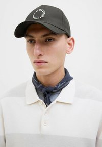 Dark cap with white logo, beige striped polo shirt with three buttons, and a blue neck scarf with white pattern. Smooth textures.