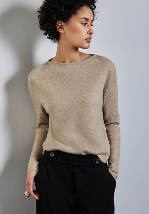 Beige, lichtgewicht trui met een bootnek en lange mouwen, gecombineerd met zwarte high-waisted broek met zilveren knopen en zakken.
