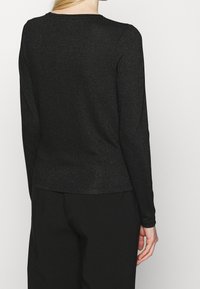 Svart långärmad topp i texturerad, skimrande tyg. Har rund halsringning och en rak nederkant vid midjan.