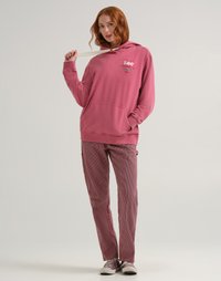 Felpa rosa con tasca frontale e coulisse, abbinata a pantaloni a righe rosse e sneakers grigie. Presenta il logo Lee in colori a contrasto.