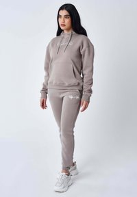 Lichtbruin hoodie met een voorzak en trekkoorden, gecombineerd met bijpassende taps toegesneden joggers. Beide hebben witte logoaccenten.