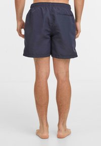 Tumši zili peldšorti ar elastīgu jostu, aizmugurējo kabatu ar rāvējslēdzēju un taisnu griezumu. Materiāls izskatās viegls un gluds.