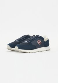 Sneakers blu navy in materiali suede e mesh, con suola in gomma bianca, caratterizzati da un patch logo rotondo e un design della punta tondeggiante.