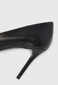 Juodas odinis aukštakulnis batelis su smailiu nosiu ir plonu stiletto kulnu. Turintis lygų paviršių ir minimalistinį dizainą.