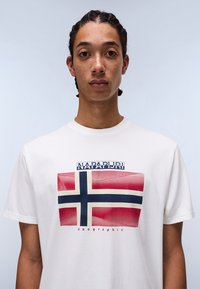 Camiseta de algodón blanca con un gráfico de la bandera noruega en colores rojo, azul y blanco. Texto "NAPAPIJRI geographic" encima del diseño.