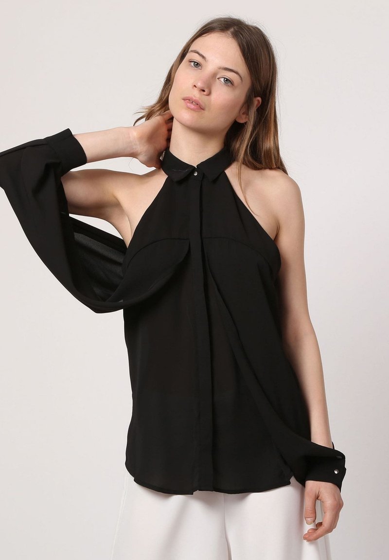 Blusa negra sin mangas con un alto cuello, diseño frontal fluido, detalle de botones en los puños y una tela suave y transparente. Se aleja ligeramente del cuerpo.