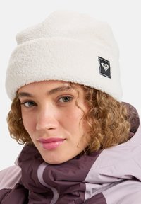 White fleece beanie with a folded brim, featuring a square black patch with a heart logo. Soft texture and warm design.