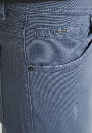 Nahaufnahme einer hellblauen Denim-Jeans-Tasche mit einem kleinen Metallschild, das im oberen Bereich "Antony Morato" liest.