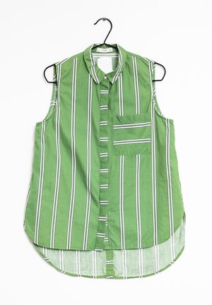 Camicia verde senza maniche con bottoni, a righe verticali bianche e una tasca sul petto, appesa a una gruccia nera.