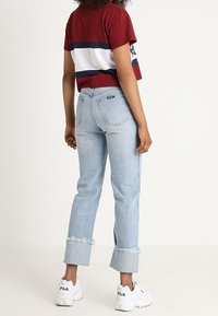 T-shirt cropped a righe rosse e bianche, jeans leggermente blu a vita alta con orli sfrangiati, e sneakers bianche Fila, viste da dietro.