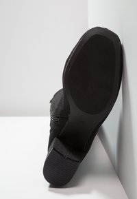 Botín negro hasta el tobillo con una parte superior de tela texturizada. Suela plana de goma con un agarre estampado, tamaño marcado como 37, detalle de cremallera lateral visible.