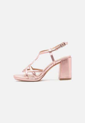 Μεταλλικό σανδάλι σε ροζ χρυσό με ψηλό χοντρό τακούνι, ανοιχτή μύτη, πολλαπλά λουριά και ρυθμιζόμενο αγκράφα στον αστράγαλο.